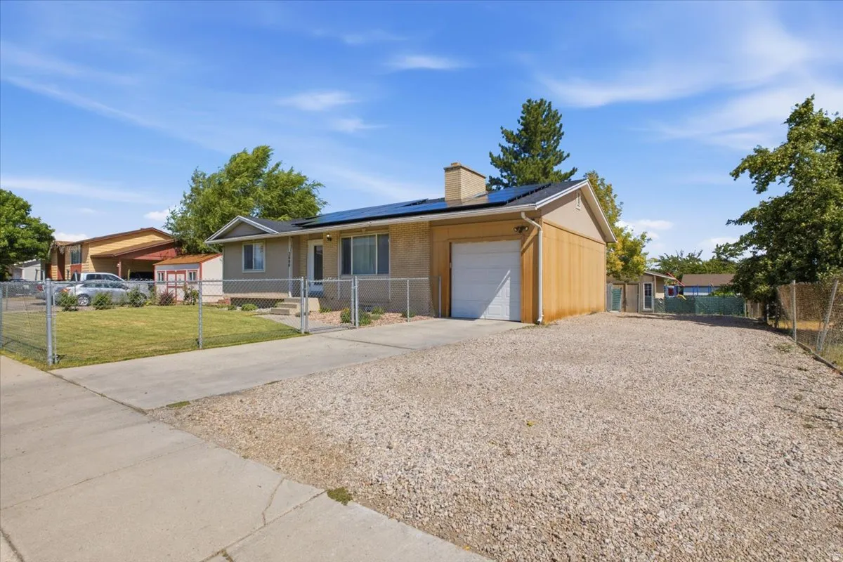 Ranch-style residence featuring a gravel side yard, a concrete driveway, an attached garage, a chain-link fence, and rooftop solar panels