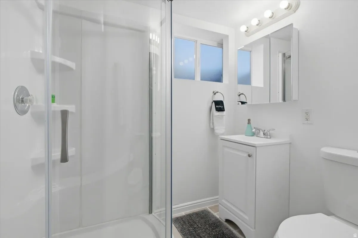 Shower with clear glass enclosure and integrated shelving, alongside a vanity featuring a white cabinet, white countertop, and a mirrored medicine cabinet