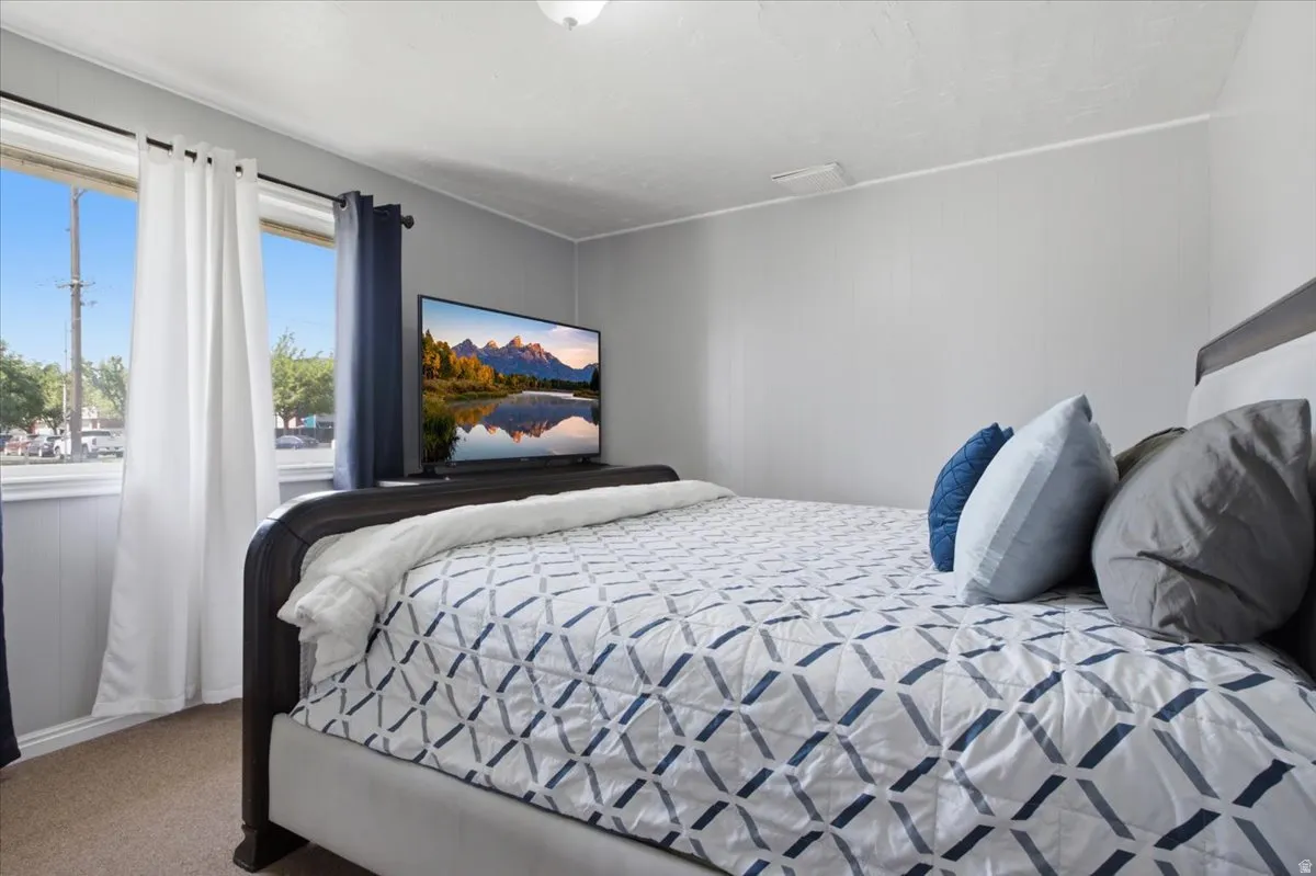 Bedroom featuring light gray wall paneling, a ceiling-mounted light fixture, and carpet flooring