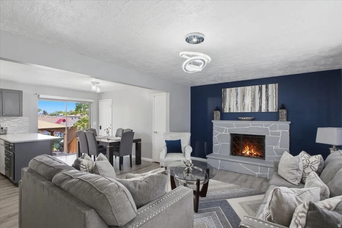 Spacious living area featuring a stone fireplace, wood-finish flooring, and a modern ceiling light fixture