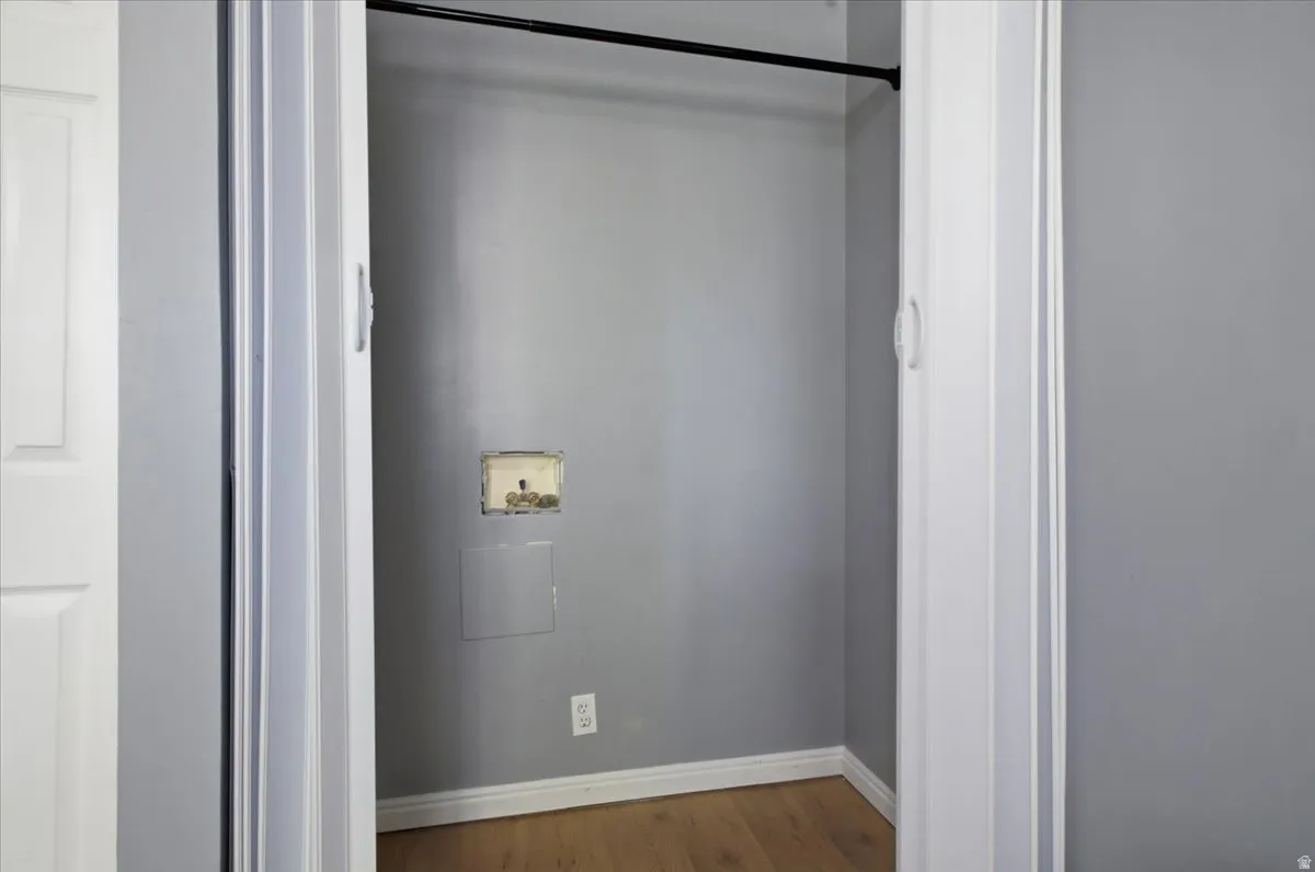 Laundry closet with wood-finish flooring, light gray walls, and white baseboards