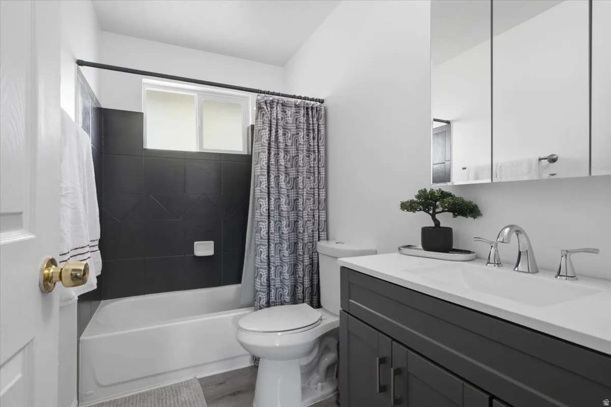 Full bathroom featuring a dark tile bath surround with an integrated window, a white tub, and a vanity with a white countertop and chrome fixtures