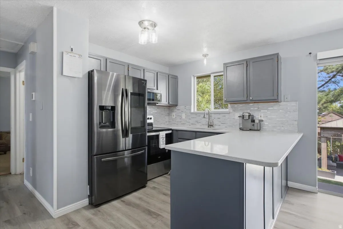 Kitchen featuring wood-finish flooring, stainless steel appliances, dark gray cabinetry, light countertops, and a white subway tile backsplash