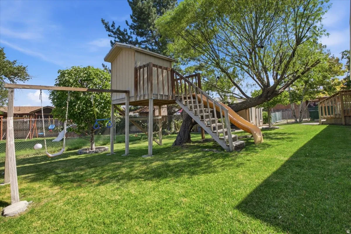 Spacious backyard featuring a treehouse with an attached slide, a swing set, and a manicured lawn