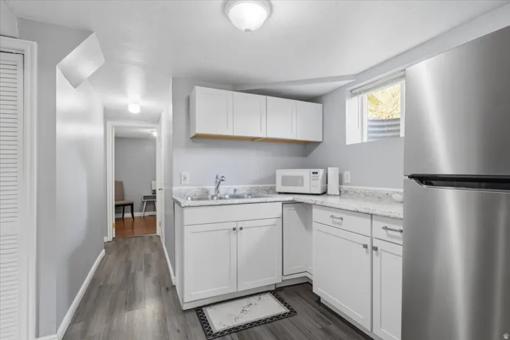 Compact kitchen area featuring white cabinetry, a stainless steel refrigerator, and wood-finish flooring