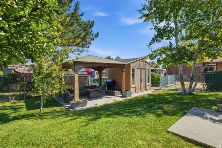 Expansive backyard featuring a central lawn, mature trees, and a concrete patio under a wooden gazebo with a metal roof