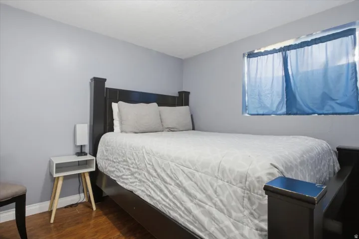 Bedroom featuring light gray wall paint, a window with blue privacy drapes, and wood-finish flooring