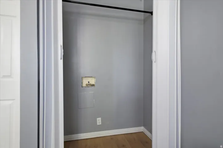 Laundry closet with wood-finish flooring, light gray walls, and white baseboards