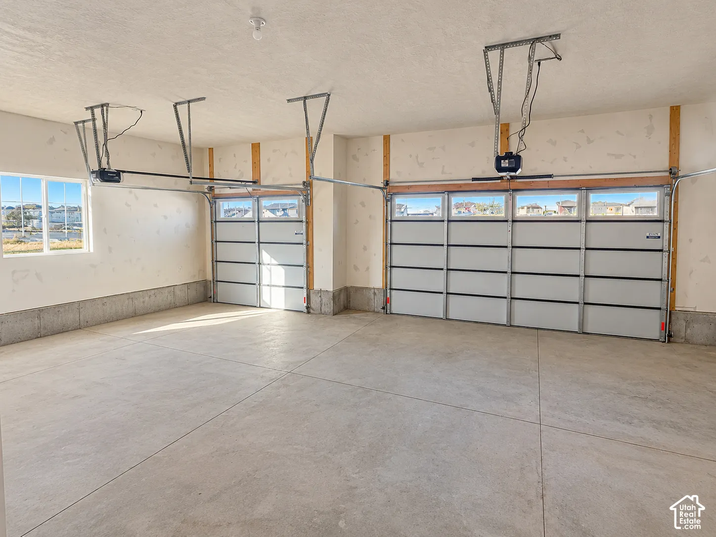 Multi-car garage featuring segmented overhead doors with glass panels, concrete flooring, exposed structural framing, and a side-mounted window