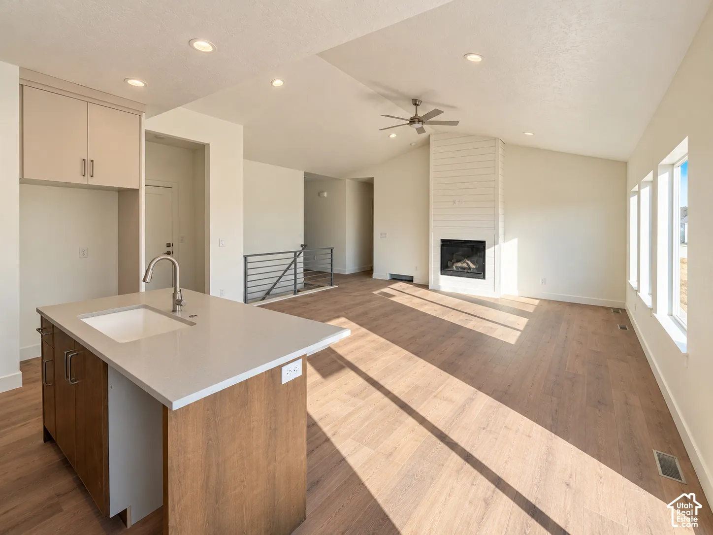 Kitchen island featuring a solid-surface countertop and undermount sink, shiplap fireplace surround, vaulted ceiling with recessed lighting, and wood-finish flooring