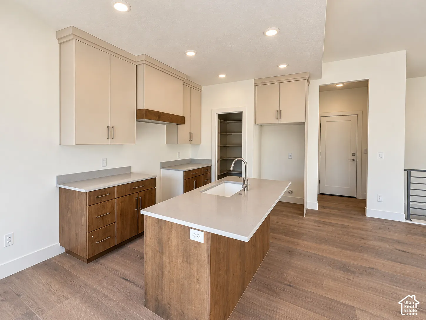 Kitchen featuring two-tone cabinetry, stone-surface countertops, a center island with an integrated undermount sink, wood-finish flooring, and a walk-in pantry