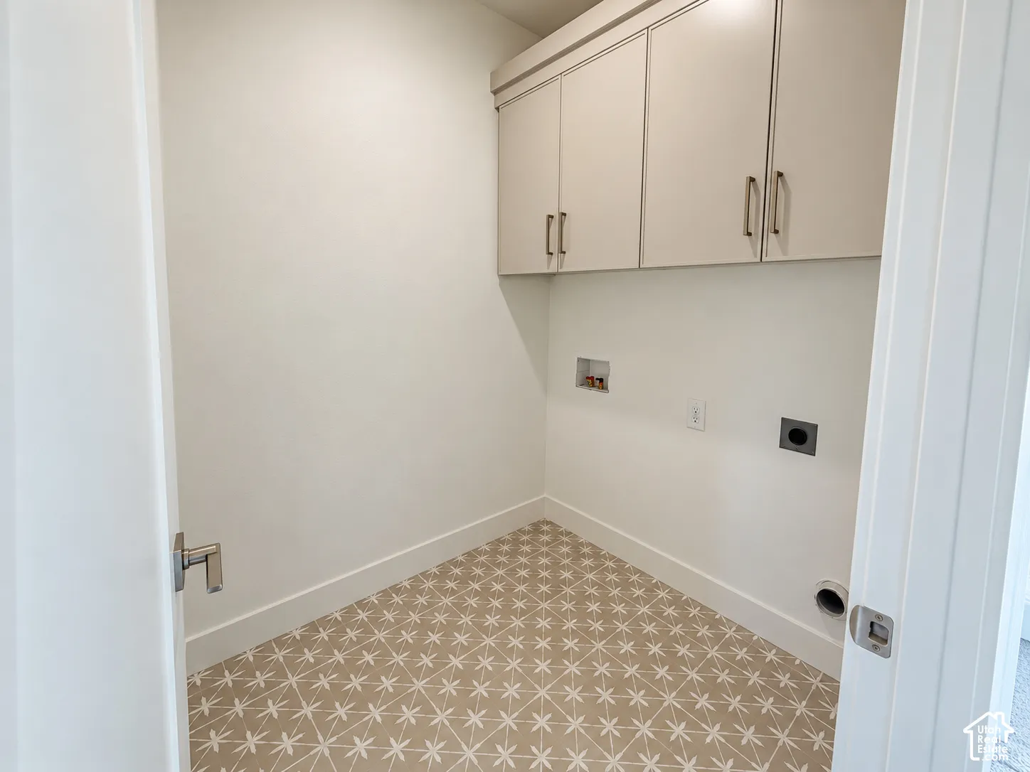 Utility room featuring upper cabinetry with metallic hardware and patterned tile flooring