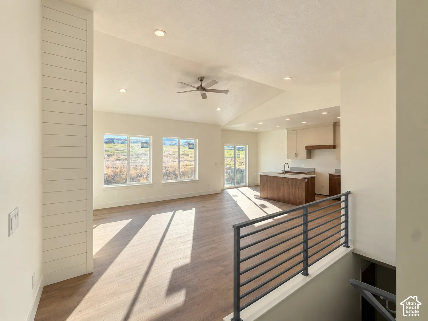 Open-concept space featuring vaulted ceilings, wood-finish flooring, recessed lighting, horizontal plank wall detailing, and a metal stair railing