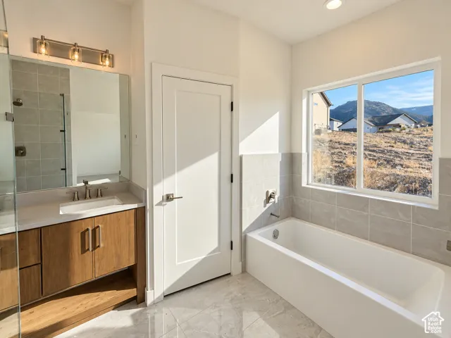 Bathroom featuring a wood-finish vanity with a stone countertop, an integrated rectangular sink, a glass-enclosed shower, a deep soaking tub with tile surround, and mountain scenery