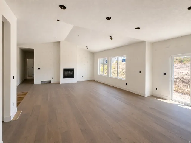 Spacious living area featuring wide plank wood-finish flooring, a modern fireplace, multiple windows, recessed lighting, and a sliding glass door