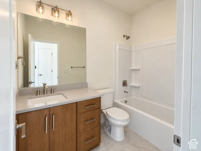 Bathroom featuring a wood-finish vanity with a stone countertop, an integrated sink, a full-width vanity mirror, and a shower-tub combination with a white surround