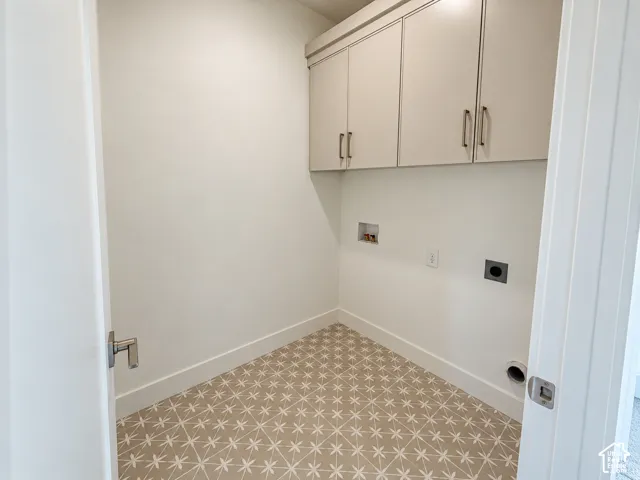 Utility room featuring upper cabinetry with metallic hardware and patterned tile flooring