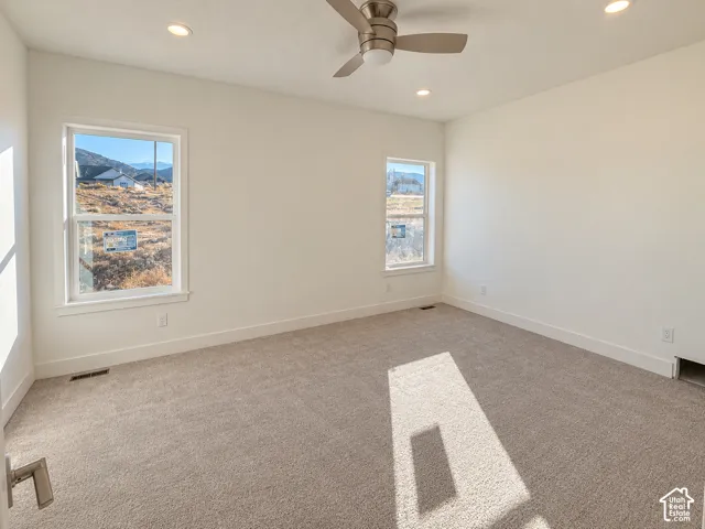 Neutral-toned carpeting, recessed ceiling lighting, brushed metal ceiling fan, and large windows with mountain scenery