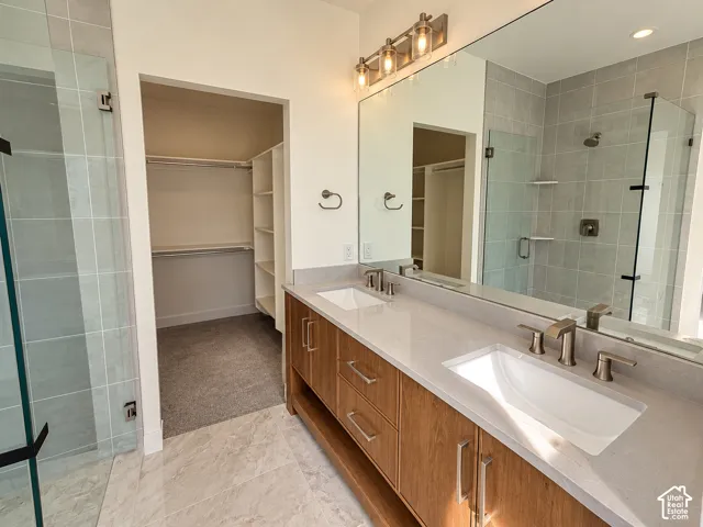 Double vanity with wood-finish cabinetry, quartz countertops, integrated sinks, glass-enclosed shower with tile surround, and built-in closet shelving