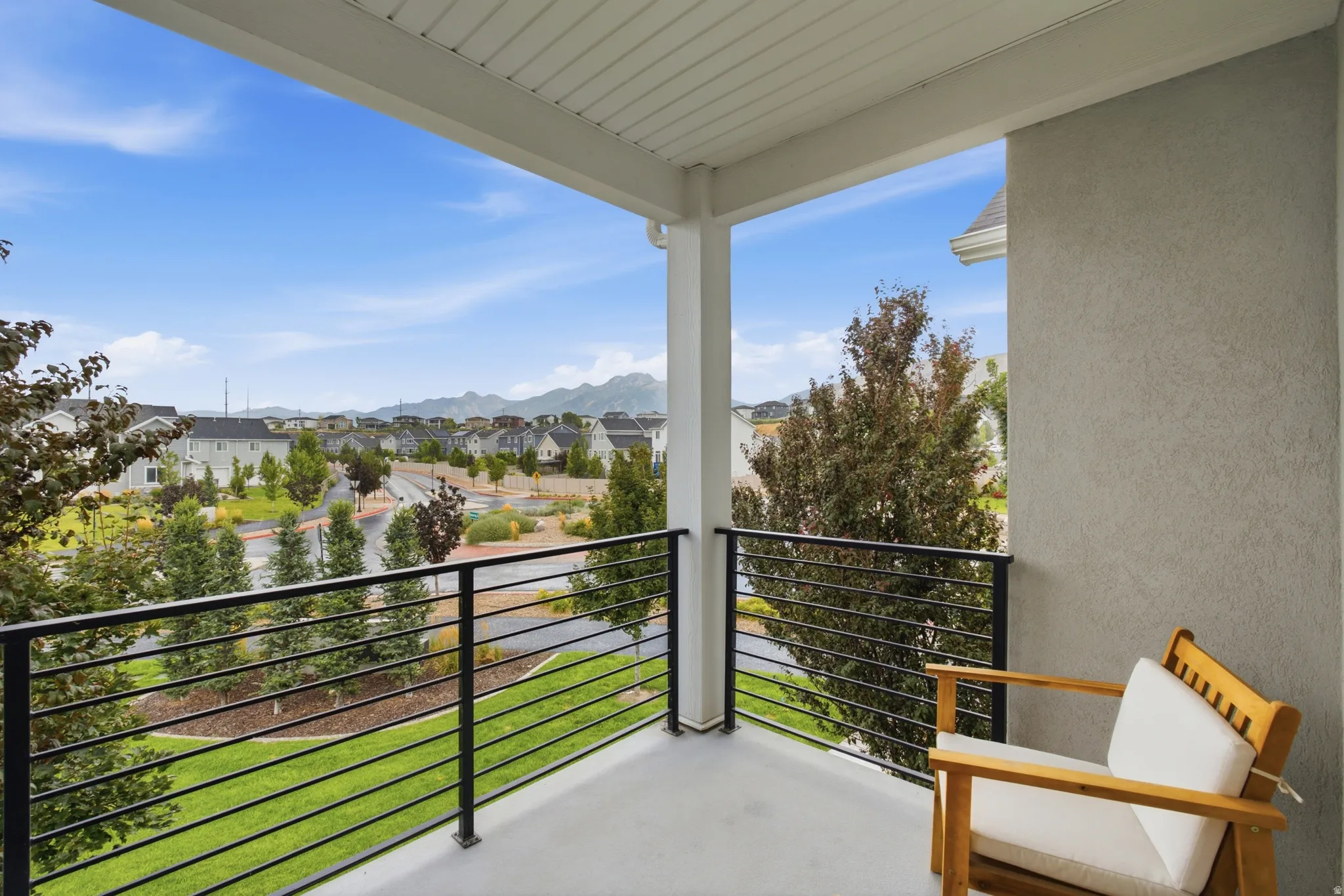 Covered balcony featuring a horizontal slat railing, textured exterior wall, and a distant mountain backdrop
