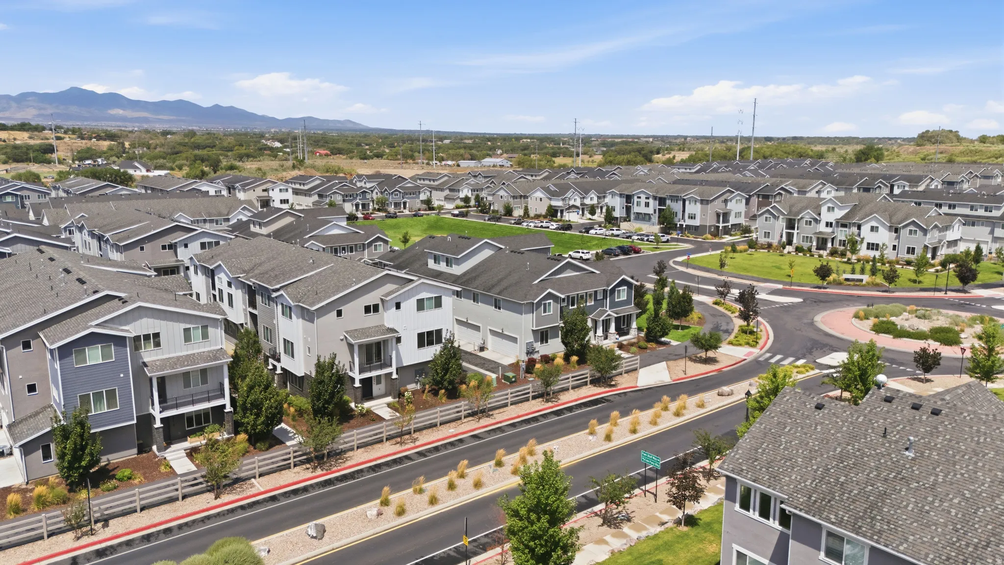 Contemporary residential development featuring multi-story homes with varied exterior finishes, a central green space, and a roundabout with landscaping