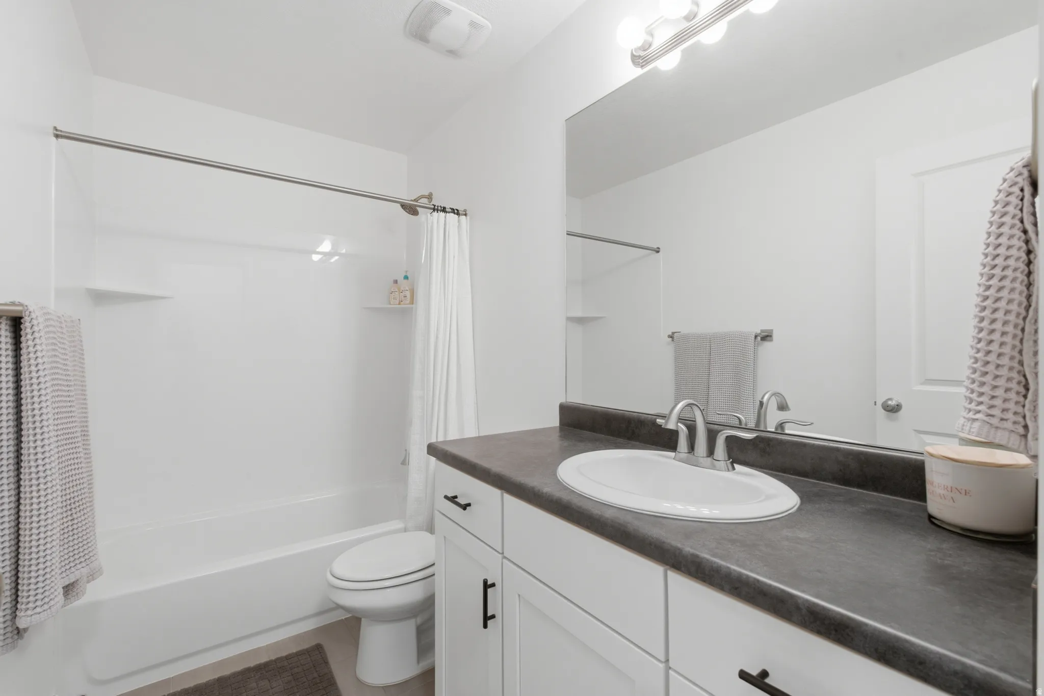 Full bathroom featuring a white tub-shower combination, a vanity with a dark countertop, white cabinetry with matte black hardware, an integrated sink with a brushed nickel faucet, and a large wall-mounted mirror