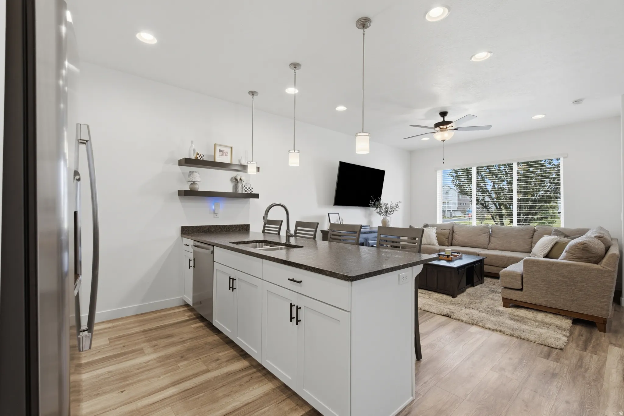 Open-concept kitchen featuring an island with integrated sink, stainless steel appliances, white cabinetry with dark hardware, and wood-finish flooring