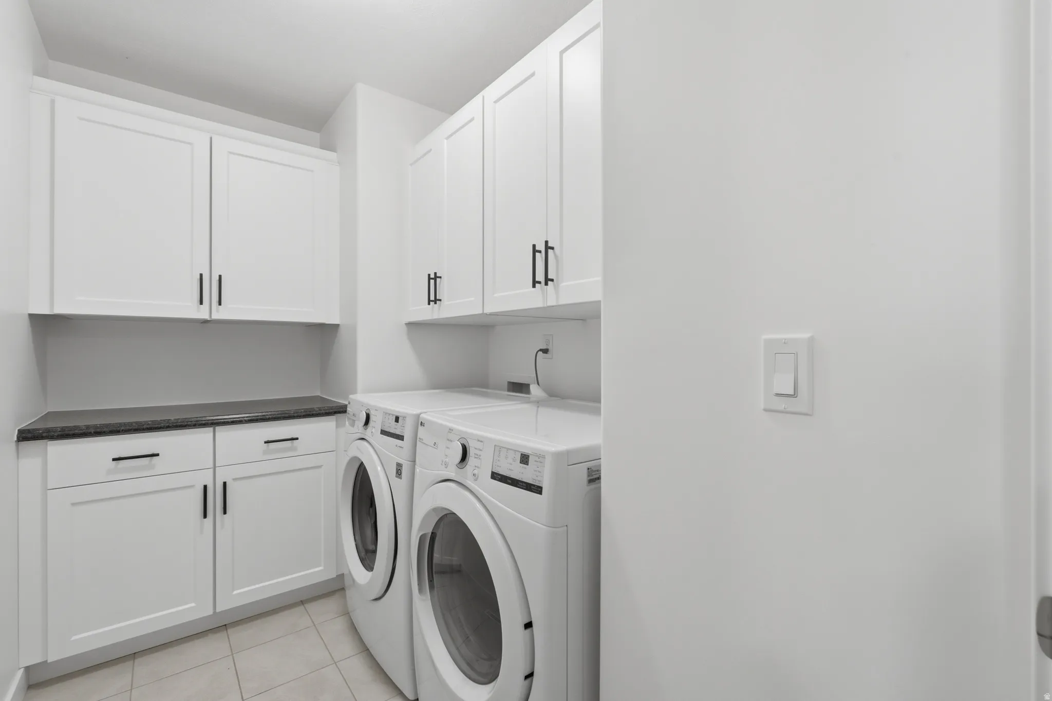 Dedicated laundry area featuring white shaker-style cabinetry, dark countertops, and tile flooring