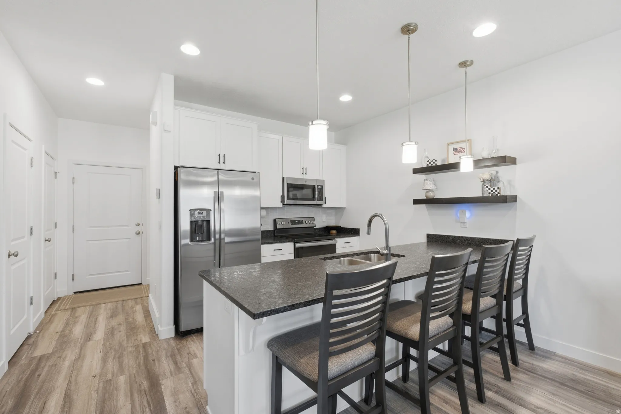 Contemporary kitchen featuring a large island with seating, stainless steel appliances, white cabinetry, and wood-finish flooring