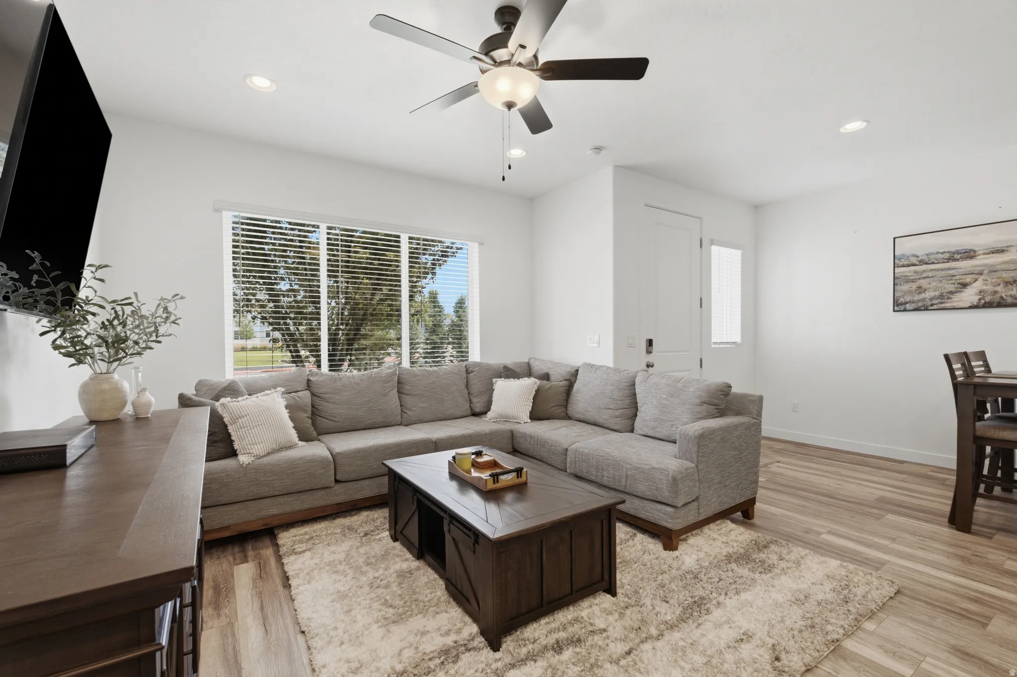 Spacious living area featuring large windows with horizontal blinds, recessed lighting, a ceiling fan, and wood-finish flooring