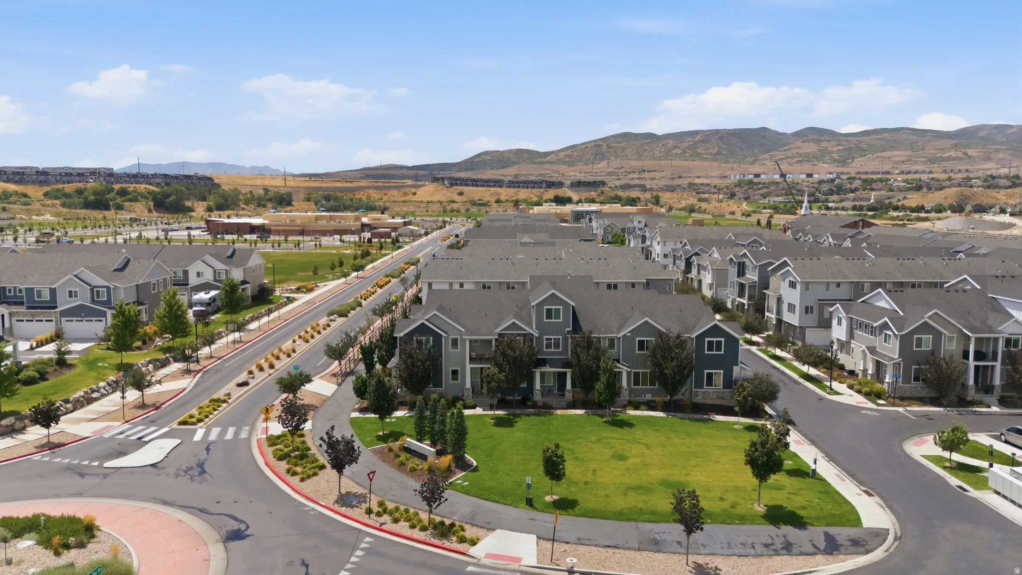 Expansive community featuring multiple residential buildings with varied siding, green spaces, paved roads, streetlights, and mature landscaping