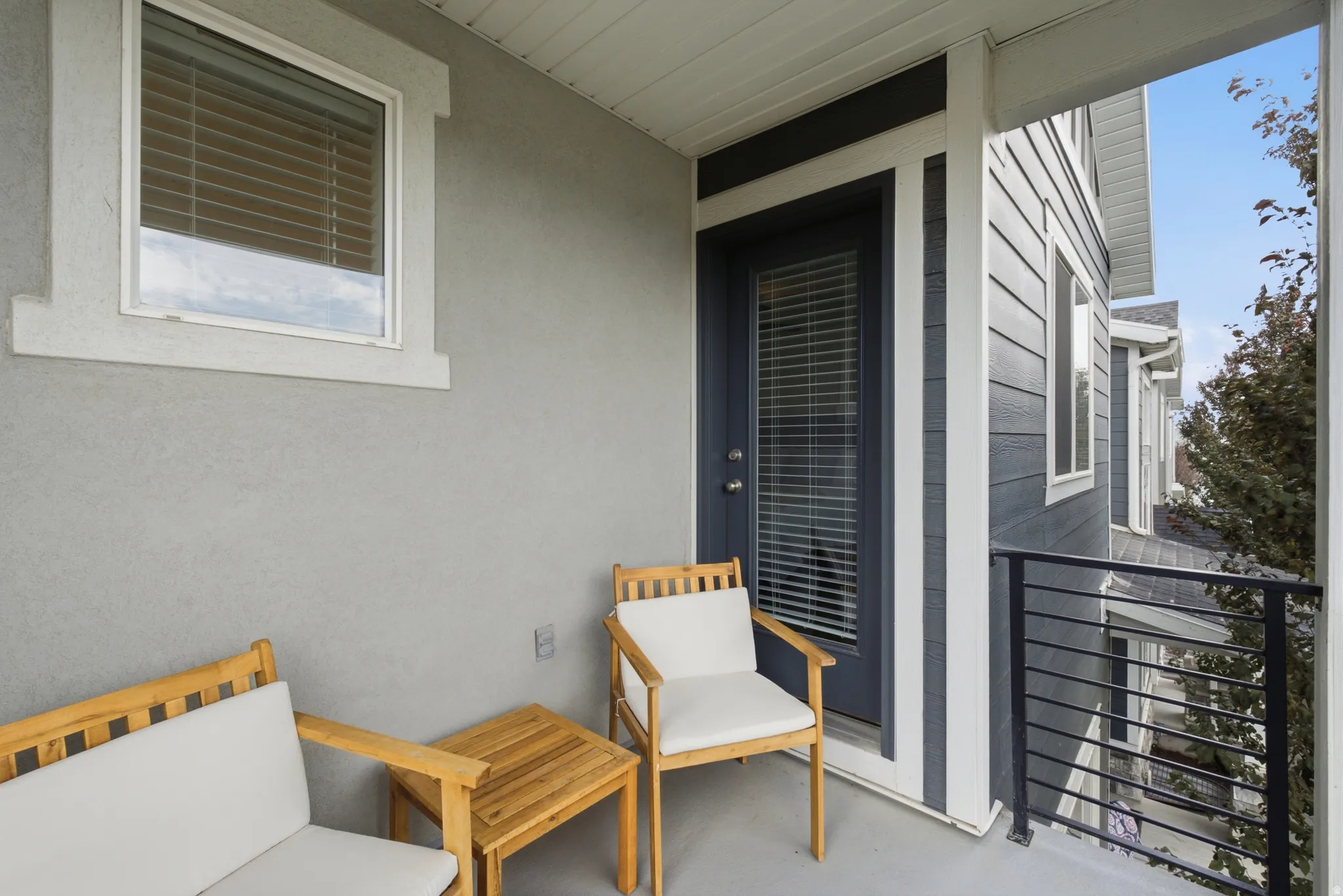 Covered outdoor balcony featuring a painted concrete floor, stucco wall, and dark-framed door with integrated blinds