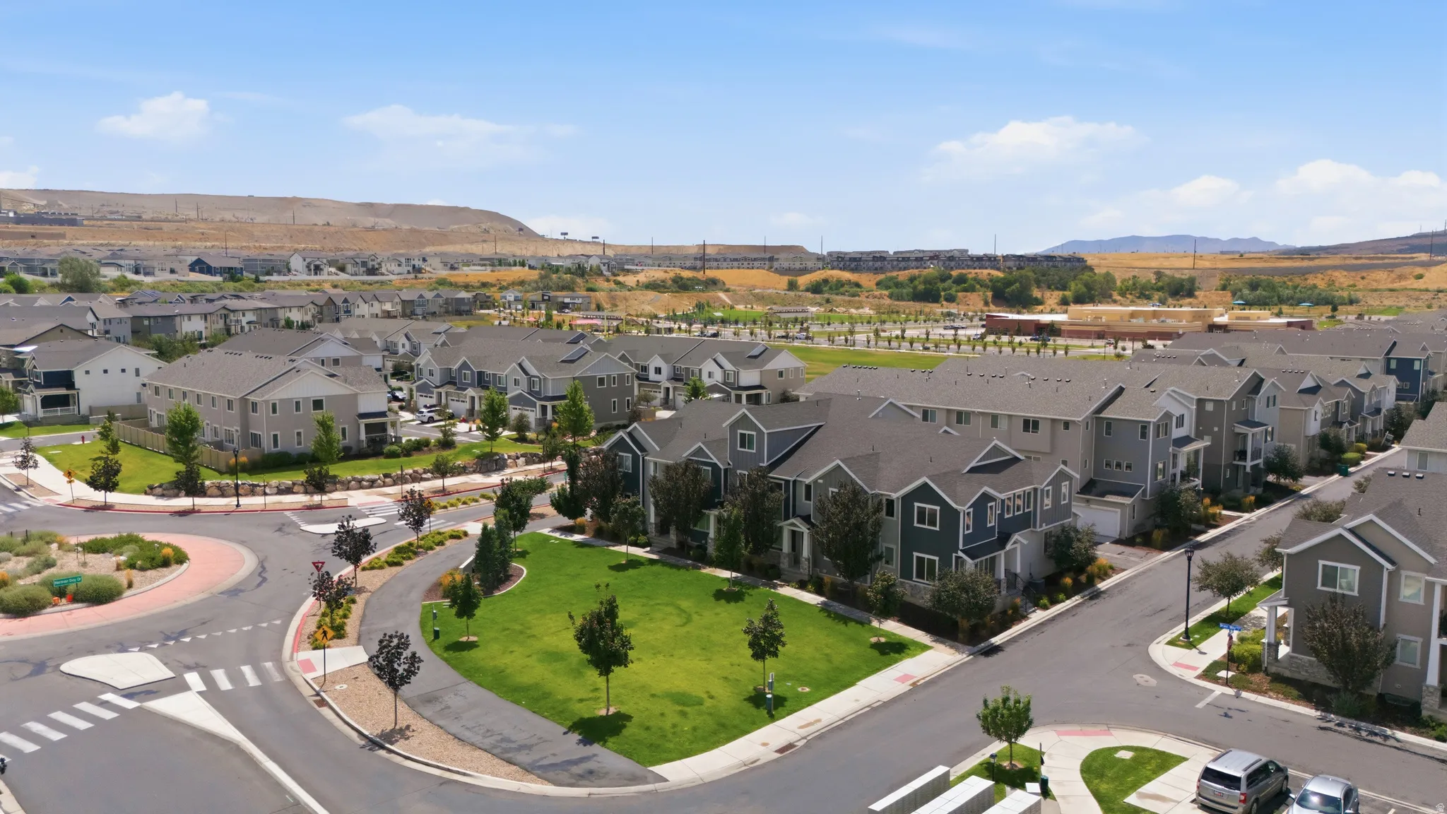 Aerial perspective of a contemporary community featuring multi-story residences with diverse siding finishes, manicured green spaces, and a circular street layout