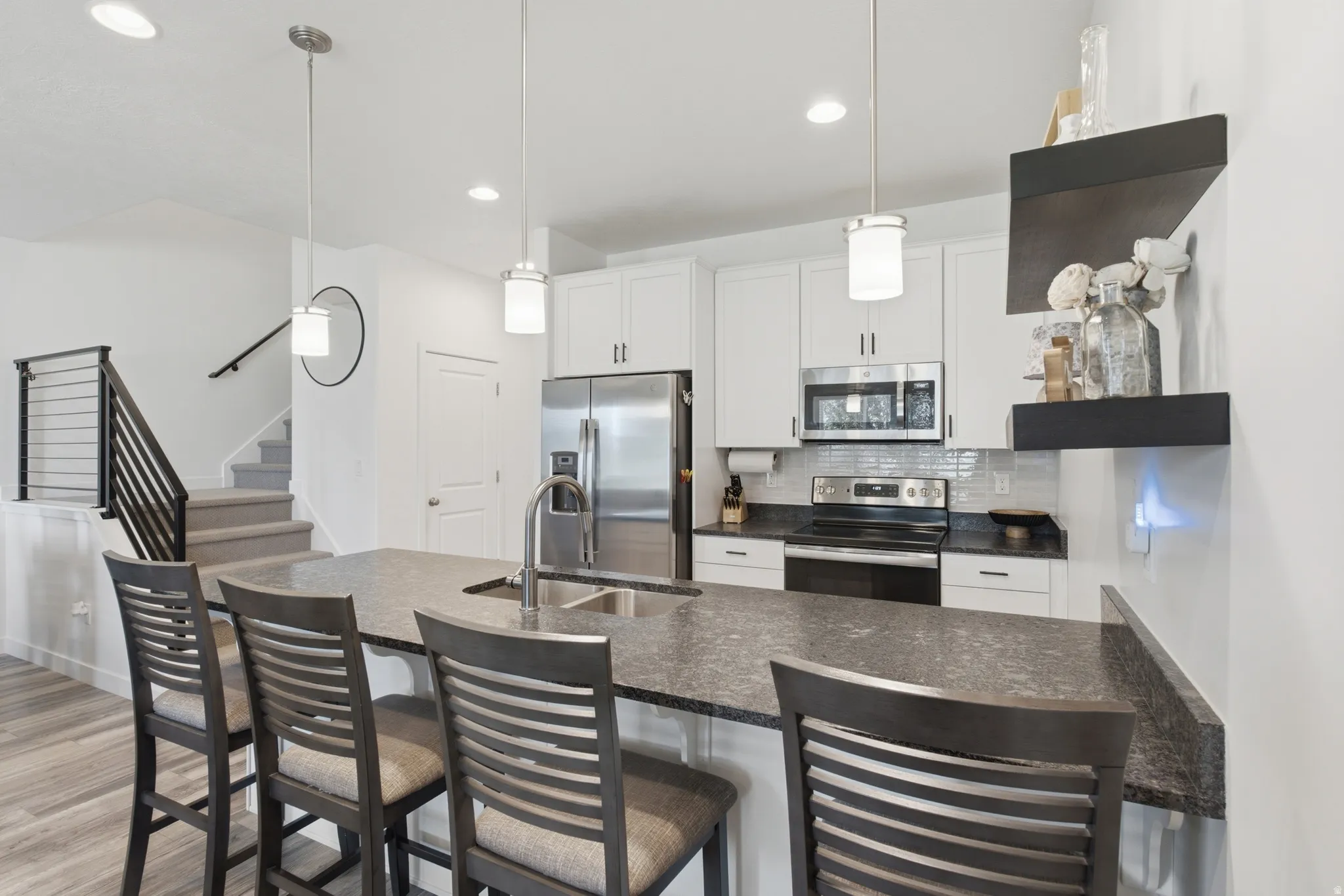 Kitchen featuring a large island with an undermount sink and seating, stainless steel appliances, white cabinetry, and a subway tile backsplash