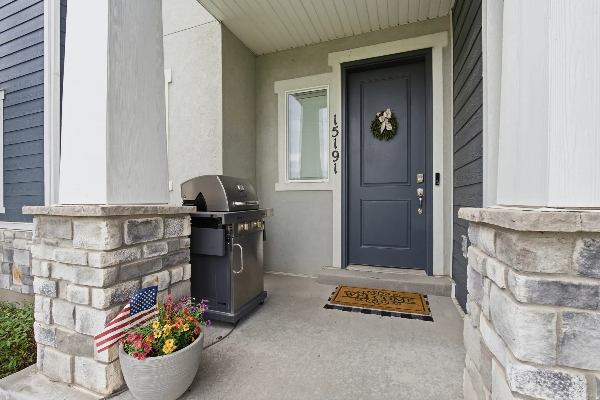 Welcoming entry featuring a paneled front door, stone veneer pillars, and horizontal siding