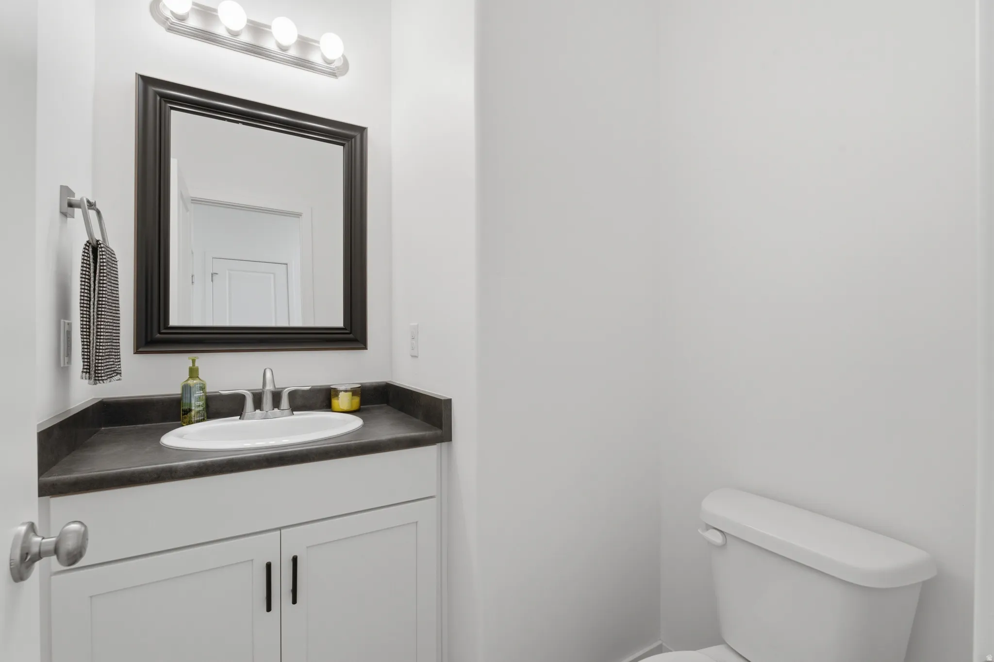Bathroom featuring a white vanity with a dark countertop, an undermount sink, a framed mirror, and a four-light fixture