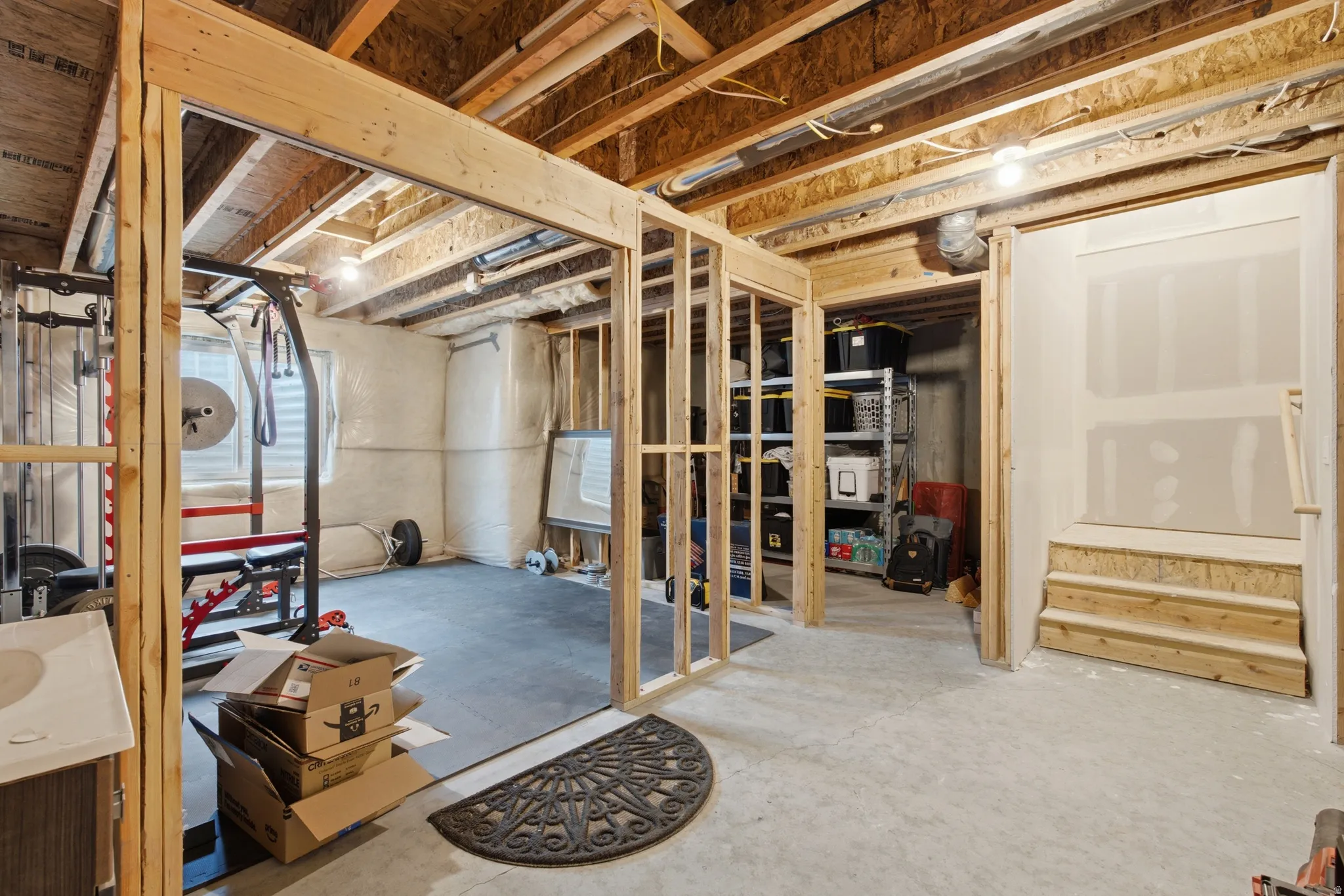 Unfinished basement space featuring exposed wood framing, concrete flooring, and partial drywall installation