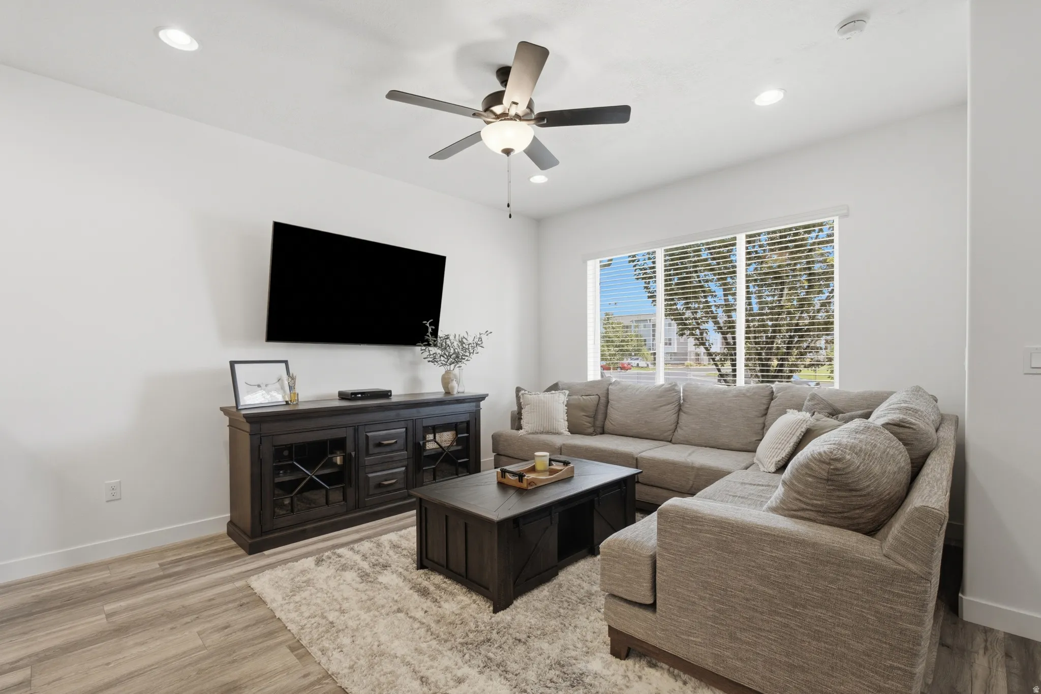 Living area featuring recessed lighting, a ceiling fan with light fixture, wood-finish flooring, and a large window with horizontal blinds