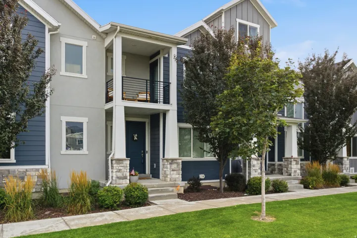 Contemporary townhome exterior featuring a contrasting blue siding and light grey stucco facade, stone accents, and a covered front entry with an upper balcony