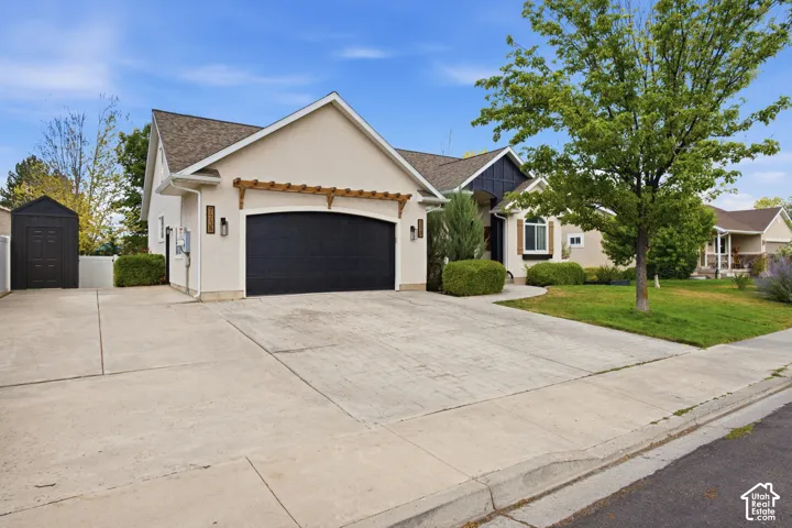 Stucco exterior with a dark garage door, decorative wood pergola, and carriage-style outdoor lighting.