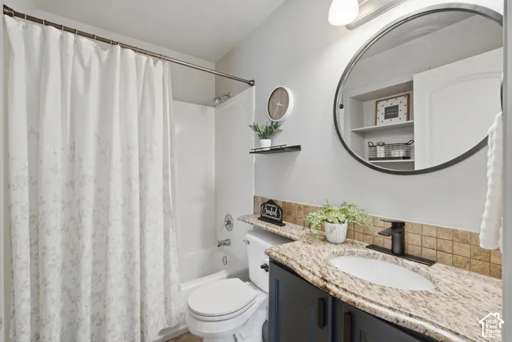 Bathroom featuring a built-in shower/tub combination, a dark vanity with a granite countertop, a circular mirror, and a tiled backsplash