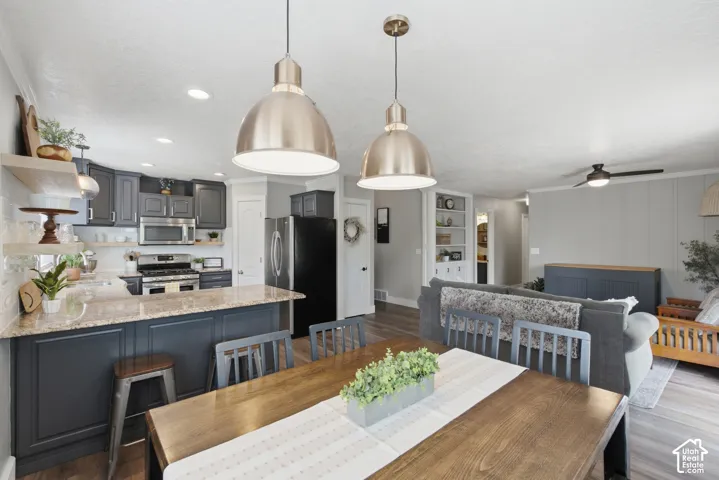 Open-concept living space featuring a dining area with beautiful pendant lights, and a modern kitchen with dark cabinetry and granite countertops.