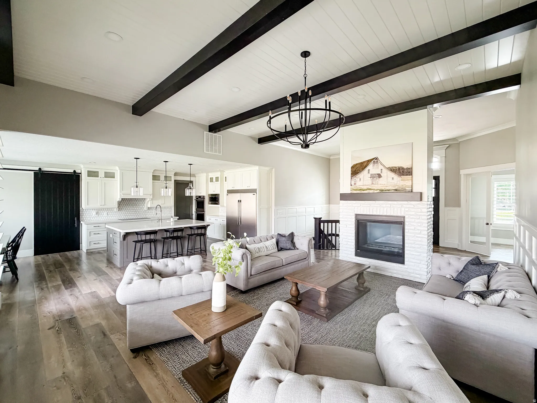 Open-concept living space featuring wood-finish flooring, a white brick fireplace with a wood mantel, and a kitchen with white cabinetry and a central island
