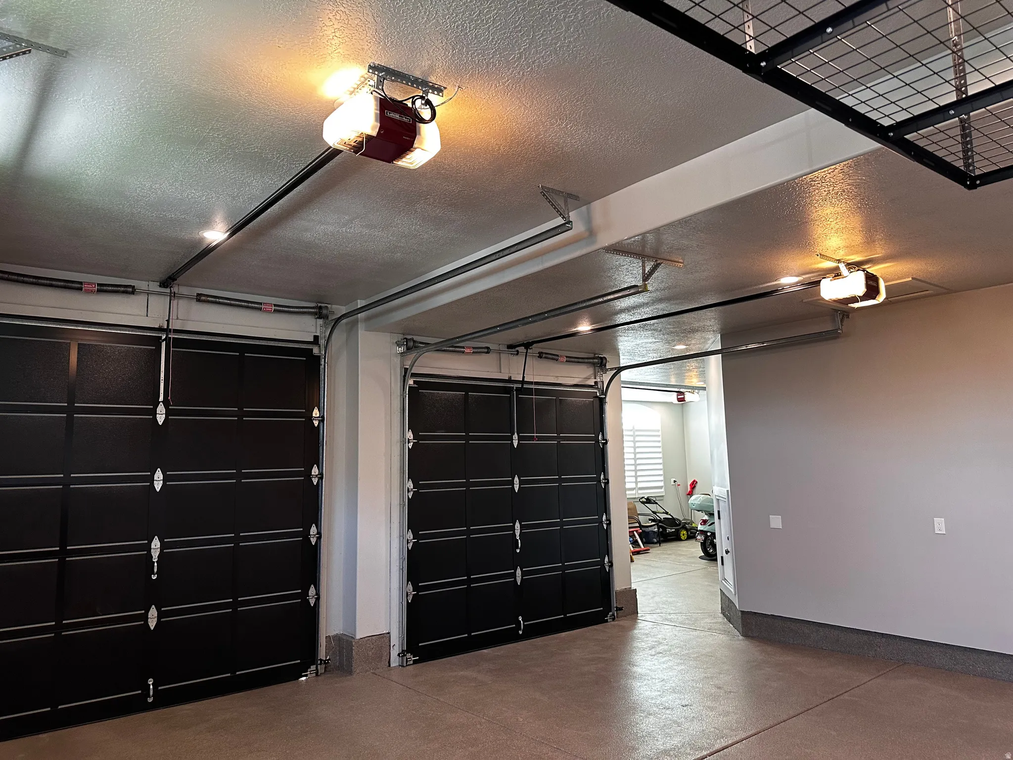 Two black garage doors with automatic openers, concrete flooring, and overhead metal storage racks