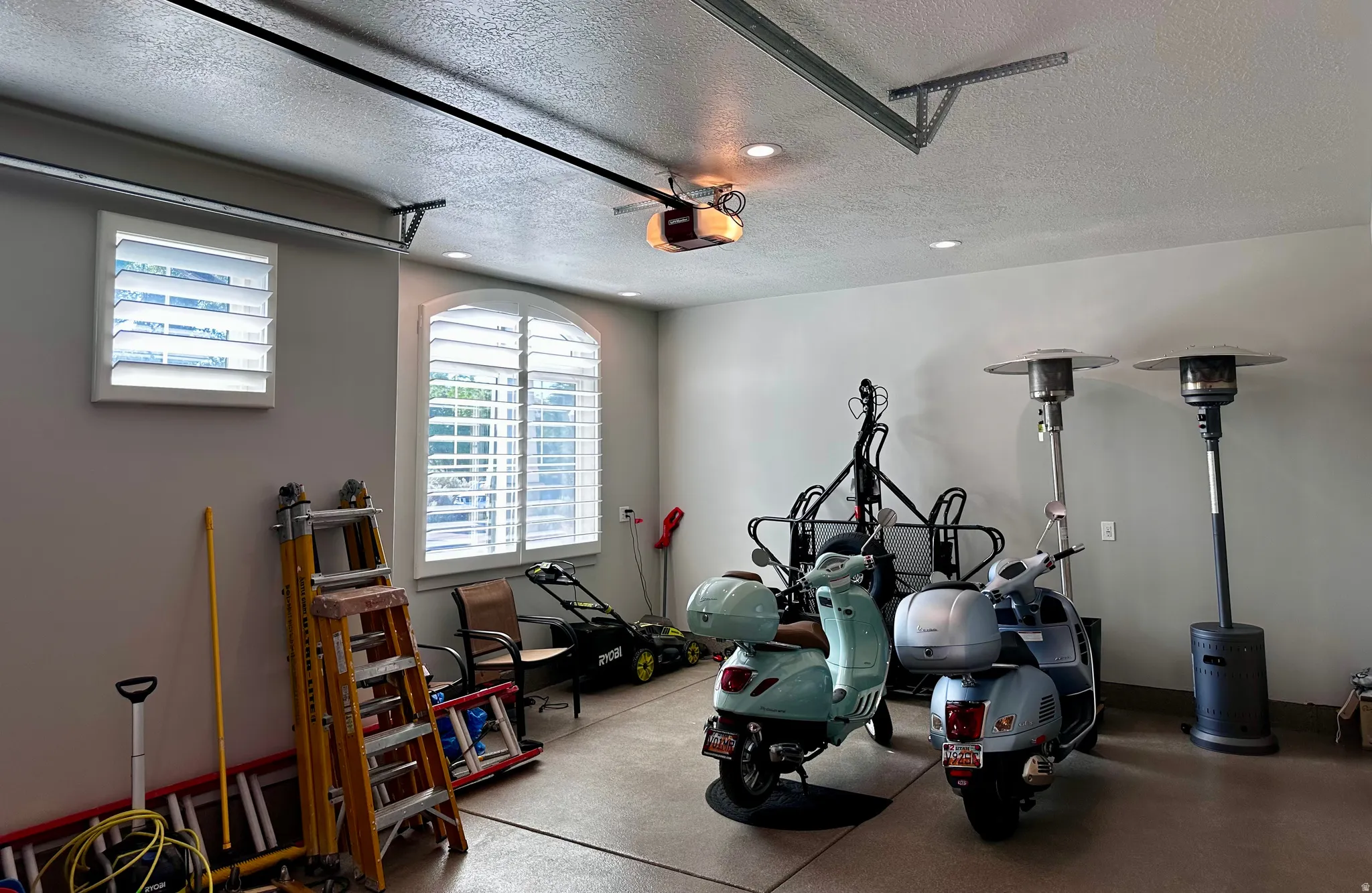 Garage featuring two windows with white plantation shutters, recessed lighting, an automatic garage door opener, and a textured concrete floor