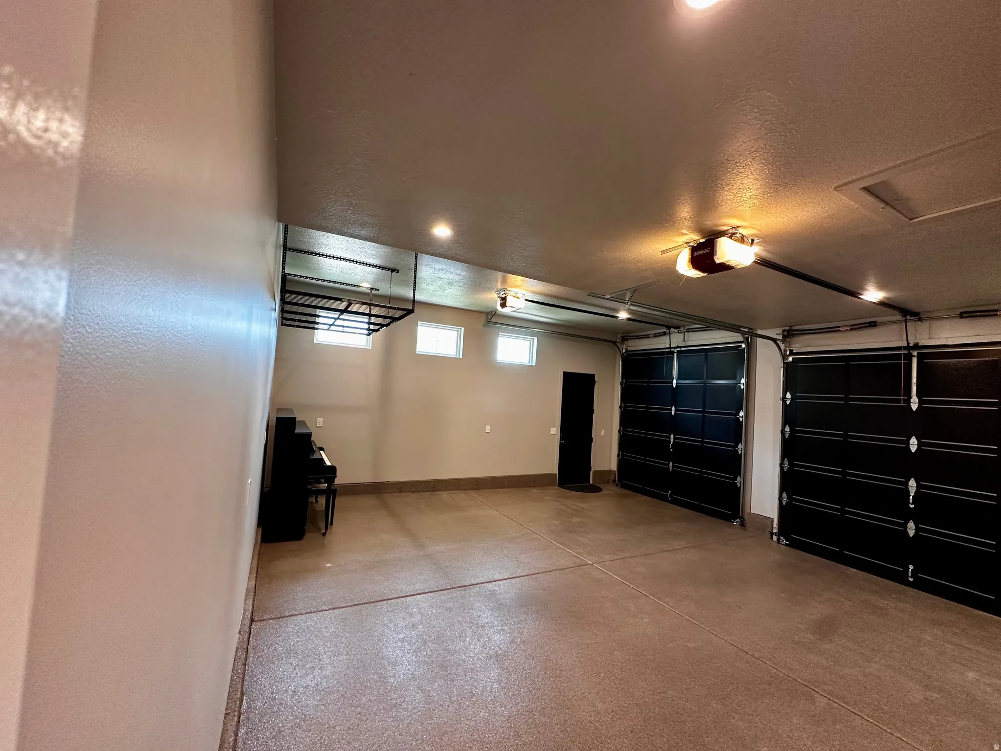 Spacious garage featuring two black overhead doors, an epoxy-coated floor, recessed lighting, and high transom windows