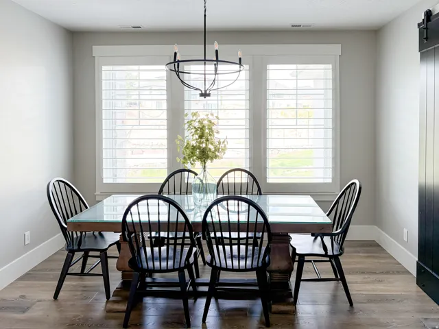 Dining space featuring three large windows with plantation shutters, wood-finish flooring, a contemporary chandelier, and a dark-paneled barn door