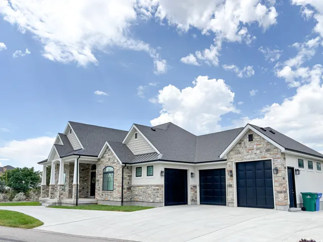 Stately exterior featuring a stone and stucco facade, dark shingle roof, and a prominent three-car garage with black doors