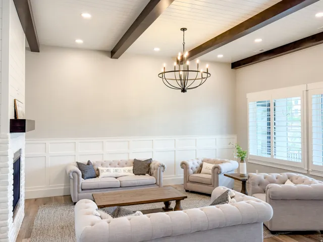 Living space featuring a white brick fireplace with a dark wood mantle, wainscoting paneling, wood-finish flooring, and a coffered ceiling with exposed beams and recessed lighting