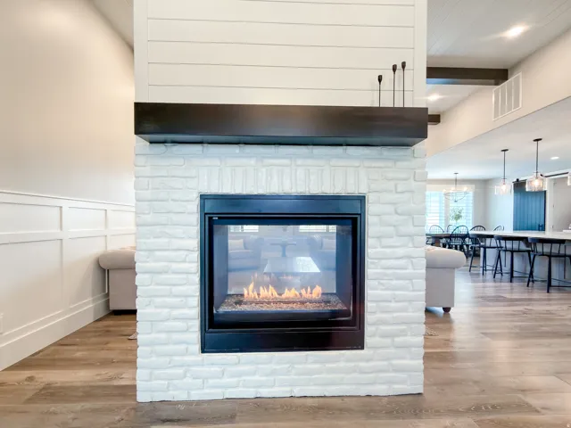 Freestanding whitewashed brick fireplace with a dark wood mantel and shiplap-style upper column